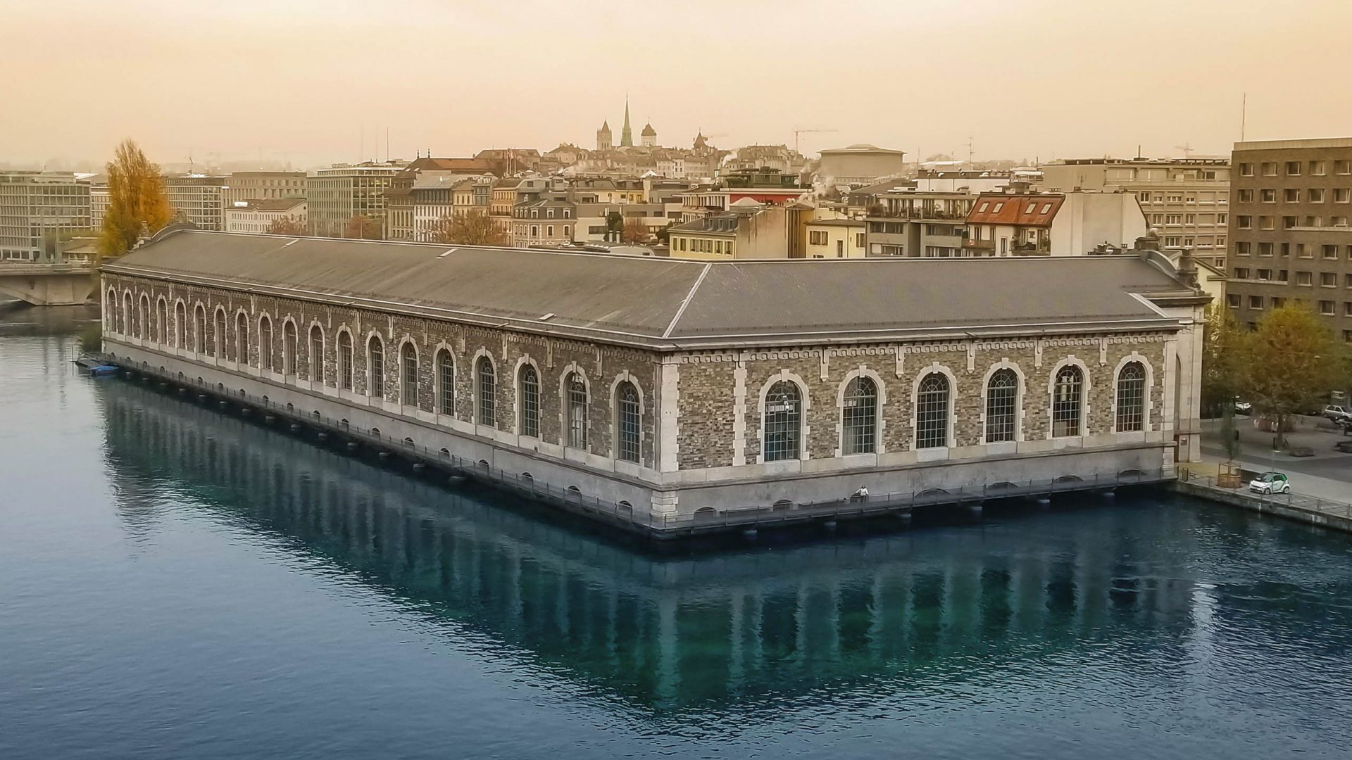 Vue du bâtiment des Forces Motrices dans son ensemble avec sa passerelle extérieure et le Rhône au premier plan